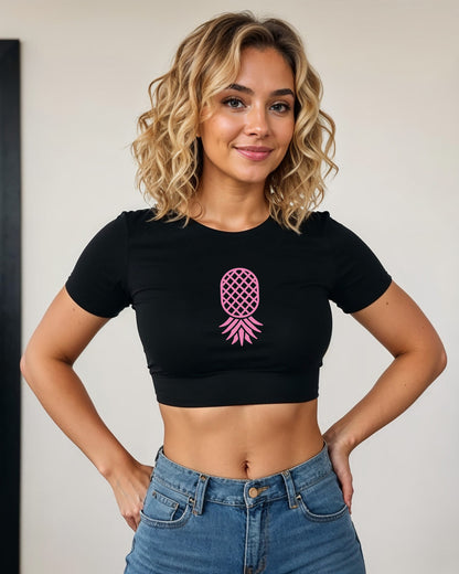 Blonde woman wearing a black crop top with minimalist pink upside-down pineapple graphic, signaling swinger lifestyle with subtle style.