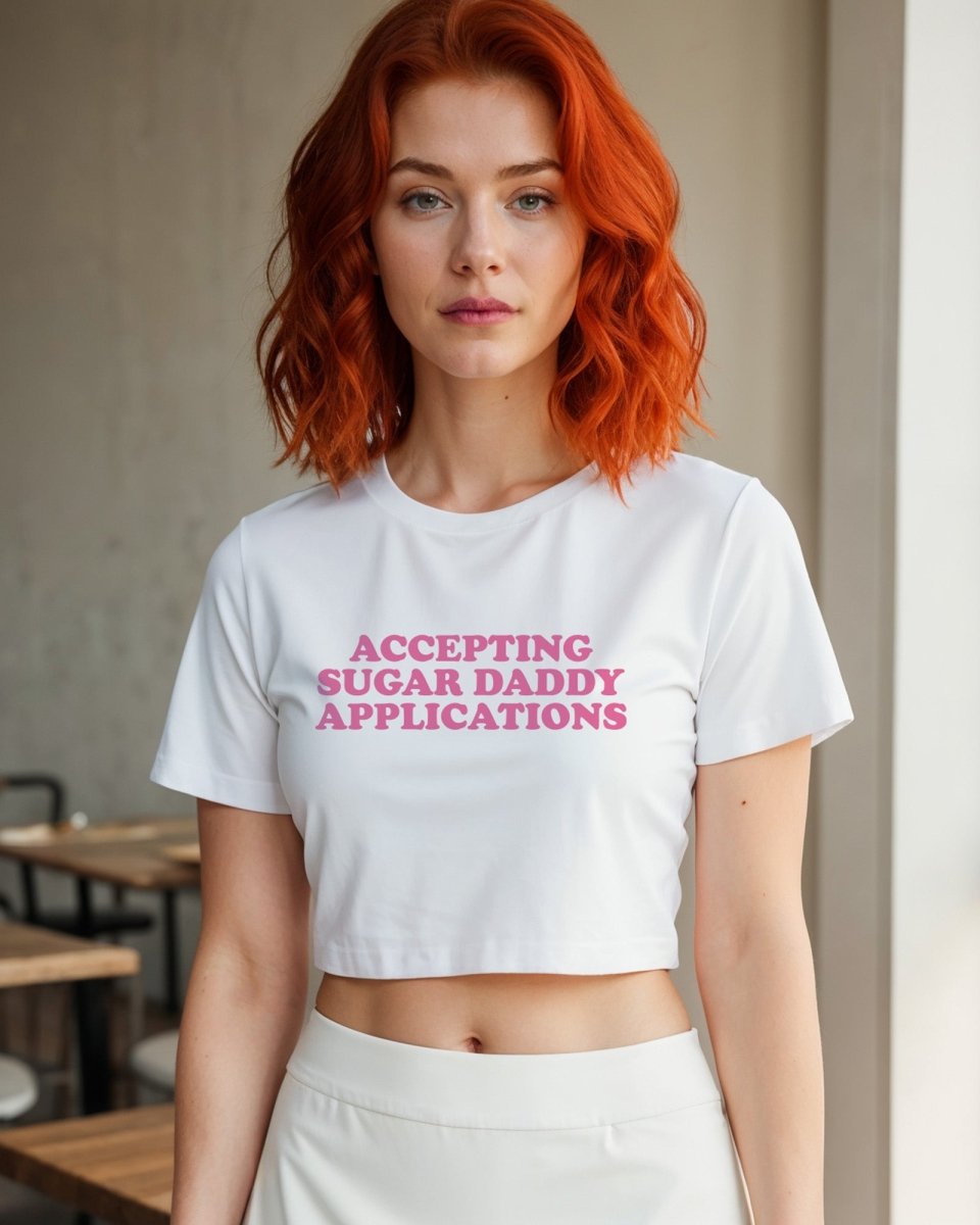 Model wearing white crop top with pink lettering that reads “Accepting Sugar Daddy Applications”