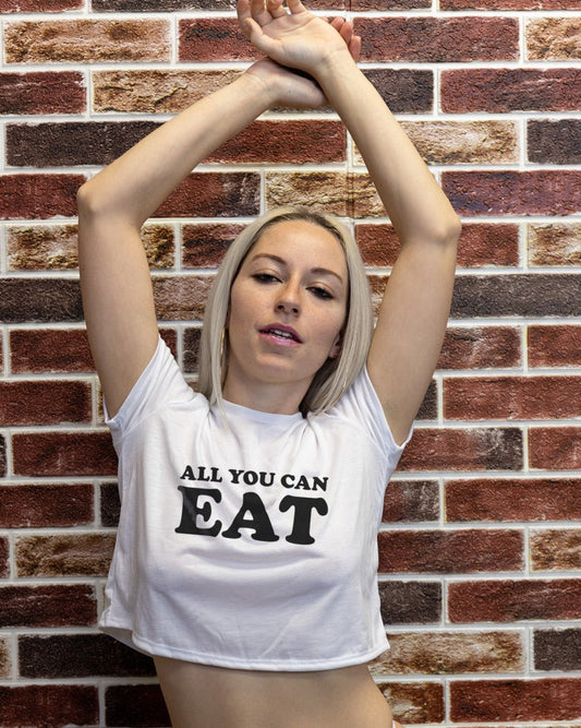 Blonde woman wearing Wicked Boutique's All You Can Eat white crop top with bold black font in front of brick wall