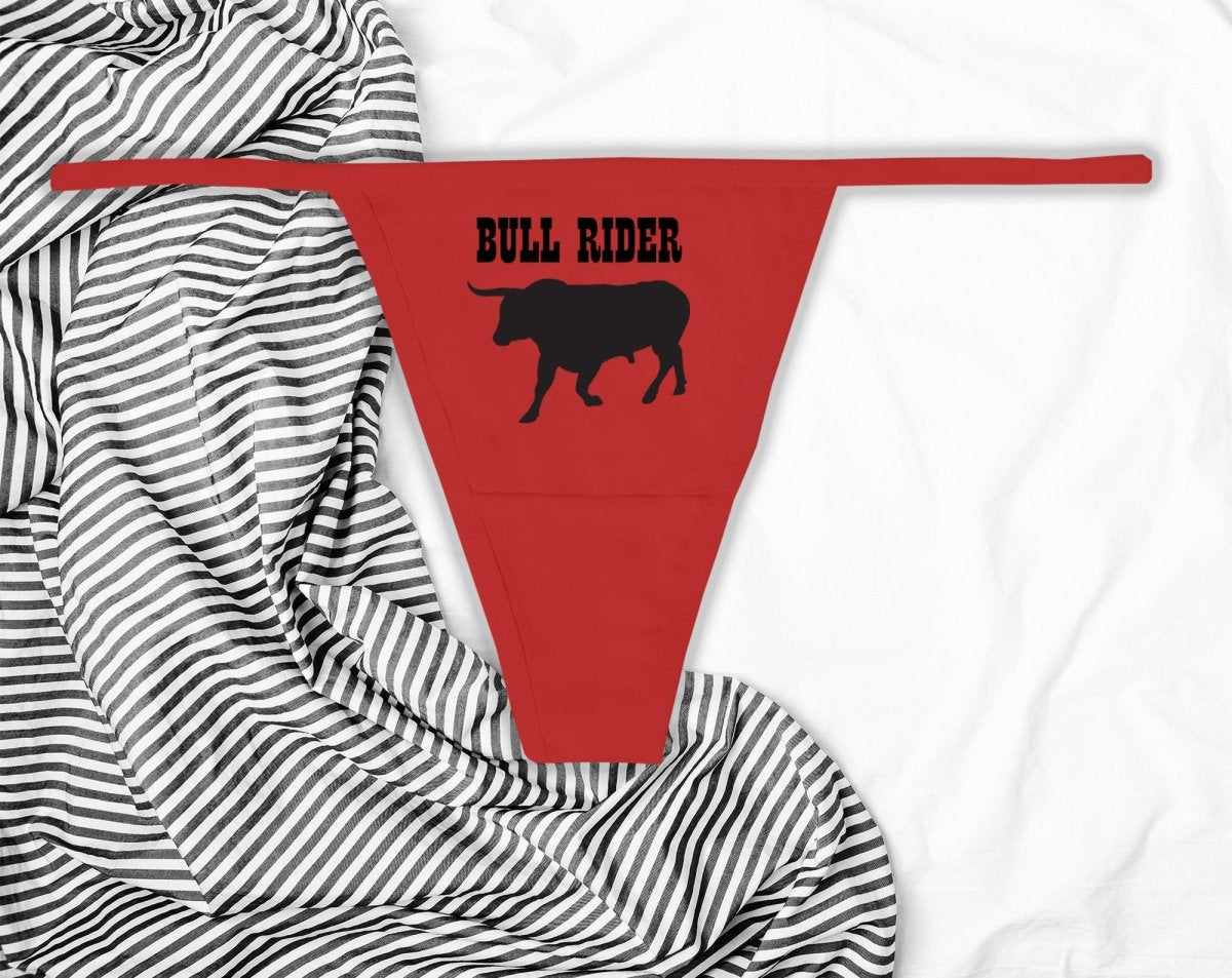 Sexy red thong with “Bull Rider” text in bold black print. Western-inspired lingerie for confident women who love to ride hard and dominate the scene.