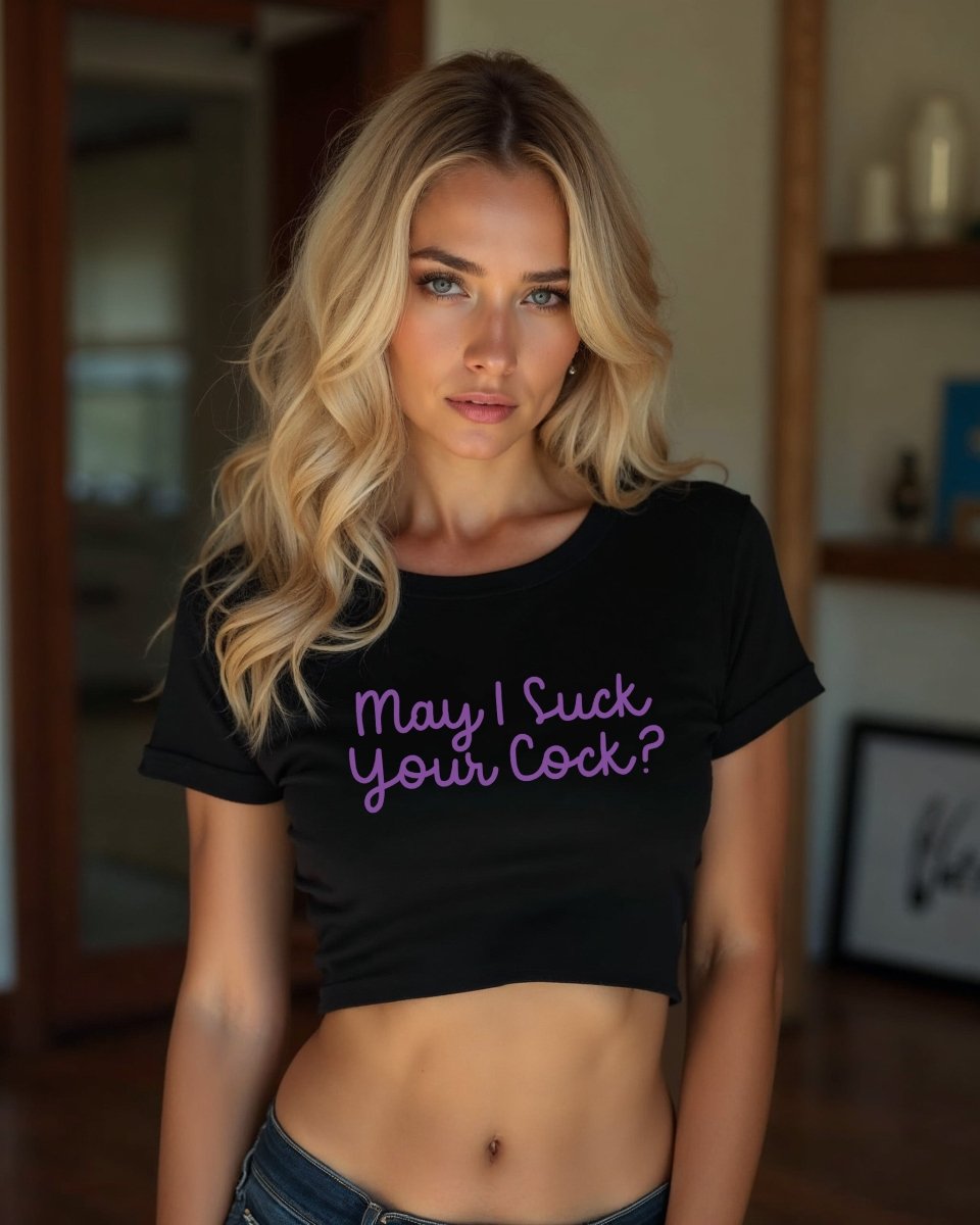 Blonde woman wearing a black crop top with “May I Suck Your Cock?” in purple text. Filthy submissive fashion for brats and obedient kink lovers.