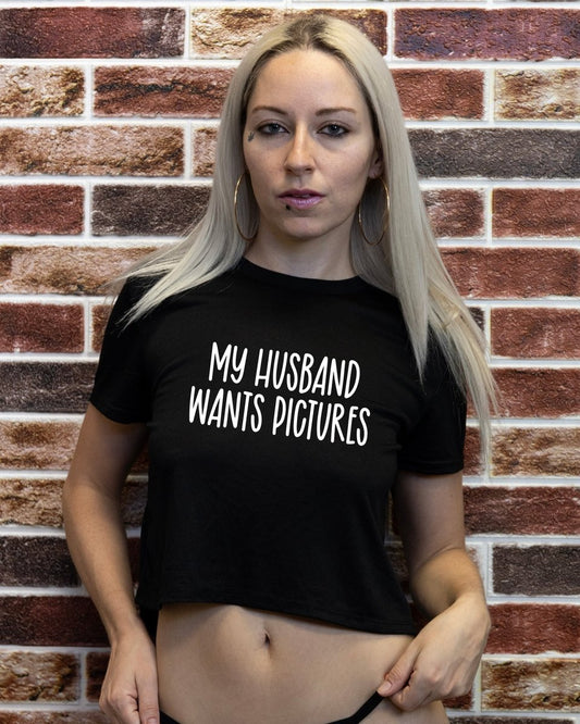 Woman wearing a black t-shirt with 'My husband wants pictures' text against a brick wall.