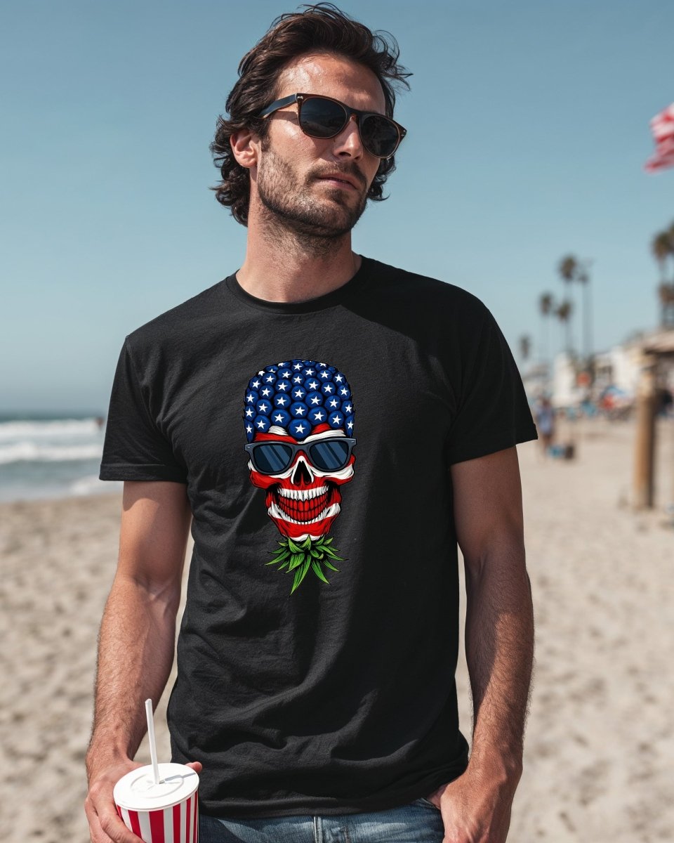 Man wearing a black t-shirt with a red, white, and blue upside-down pineapple skull graphic. Bold patriotic design for edgy summer fashion.